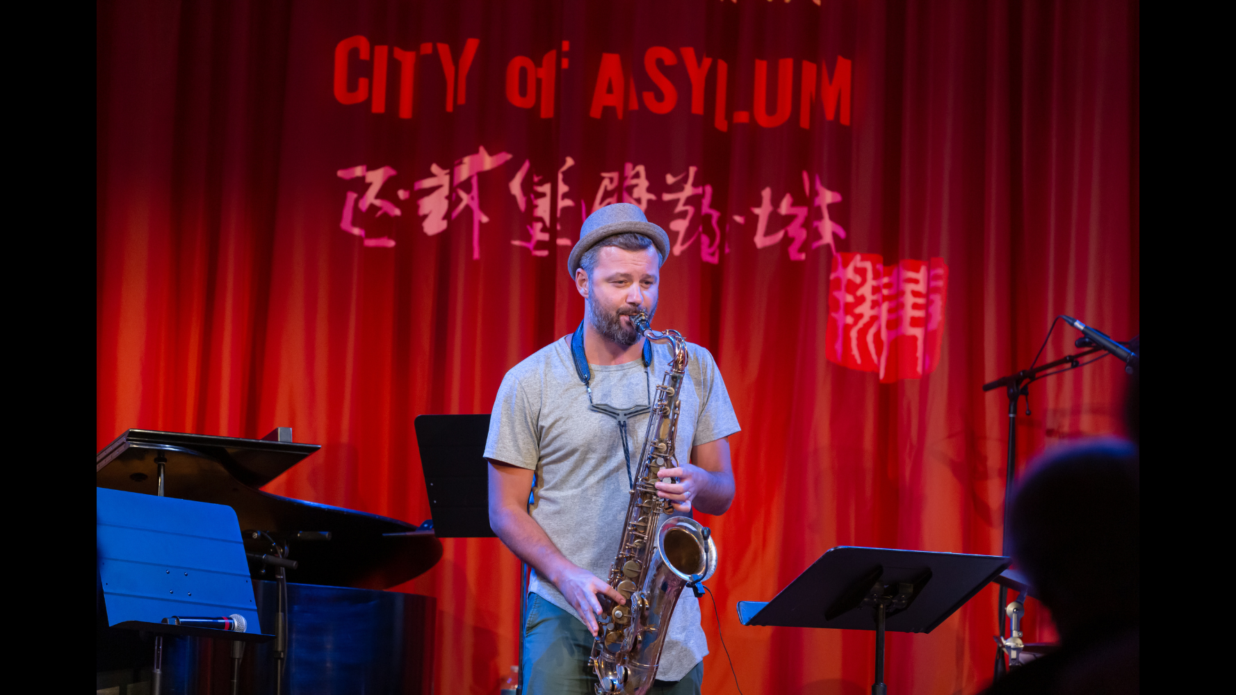 Image of musician playing tenor saxophone on a stage with other instruments in background